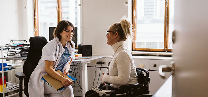 En kvinnlig läkare pratar med en kvinna som sitter i rullstol.