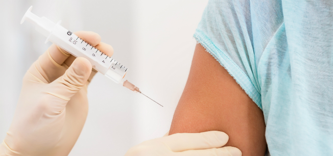 En persons händer med handskar på håller i en spruta och ger vaccination i en annan persons överarm.