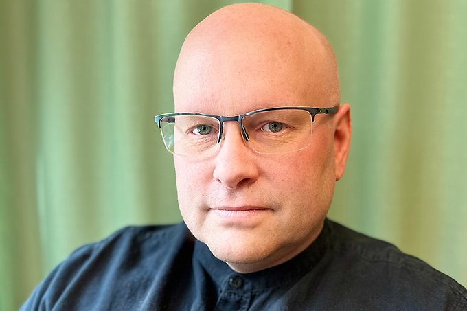 Ansiktsbild på en person i blå skjorta, glasögon och snaggad frisyr.