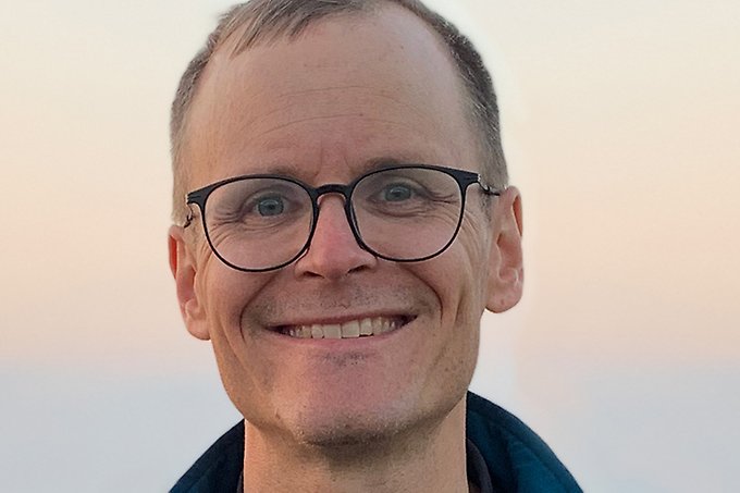 Leende person med kortklippt frisyr och glasögon tittar in i kameran