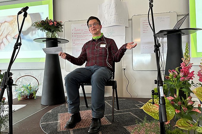 En person sitter på en stol på en scen och slår ut med armarna