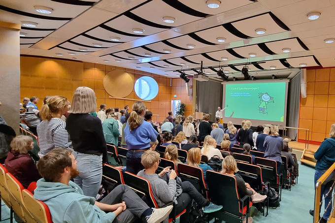 en person föreläser på en scen i en fullsatt hörsal
