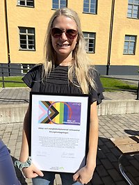 en person står utomhus i soligt väder och håller i ett diplom för hbtqi-diplomering
