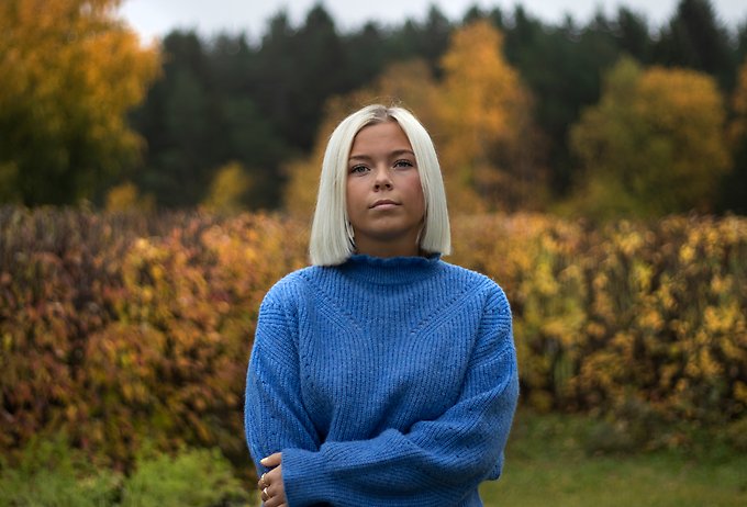 Halvkroppsbild utomhus på en person med blå tröja och ljust, axellångt, rakt hår.